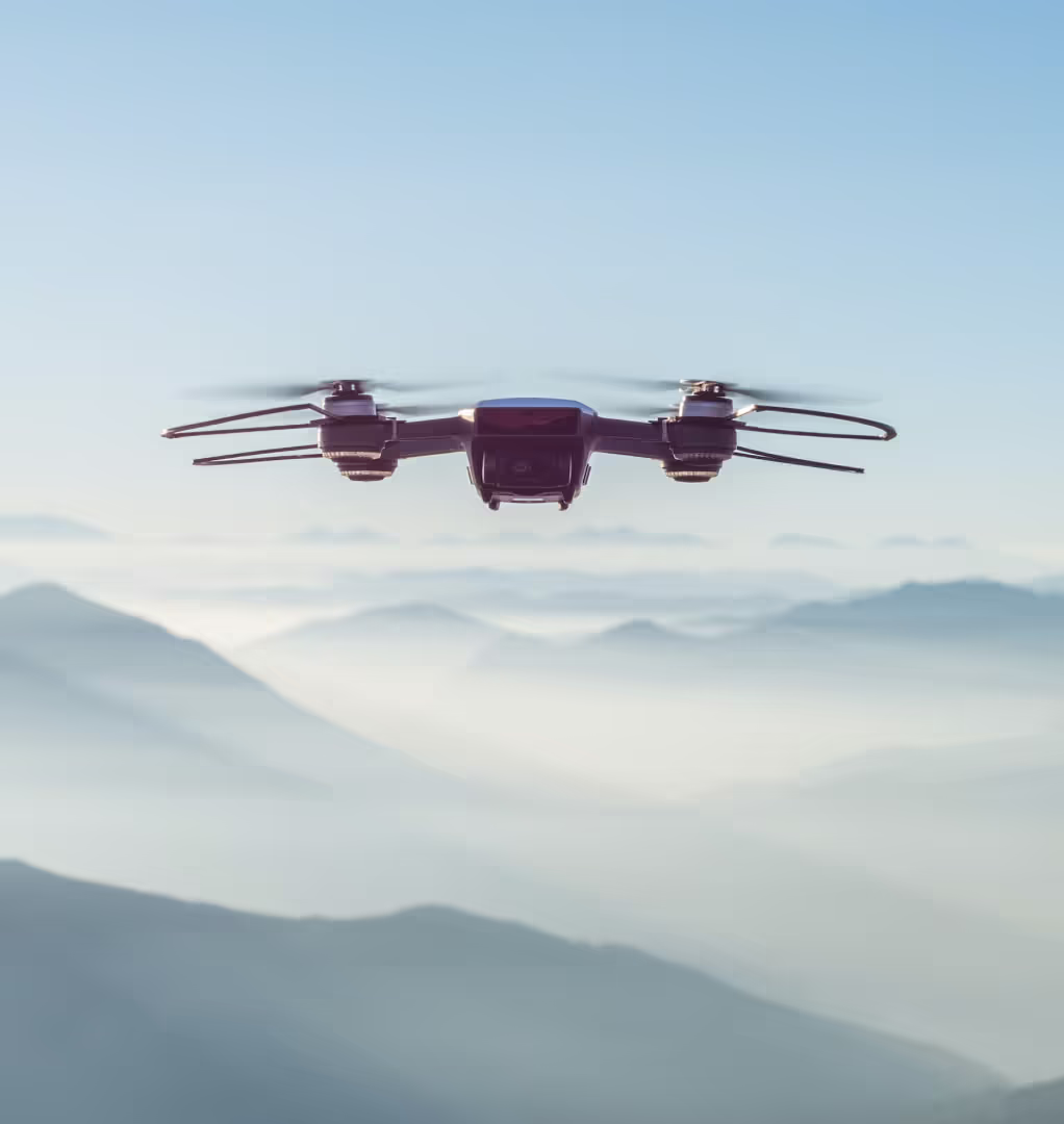 A drone hovers with a view of mountains behind it.