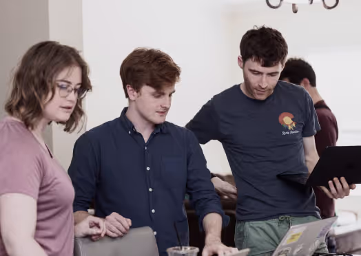 Three team members reviewing code on a laptop