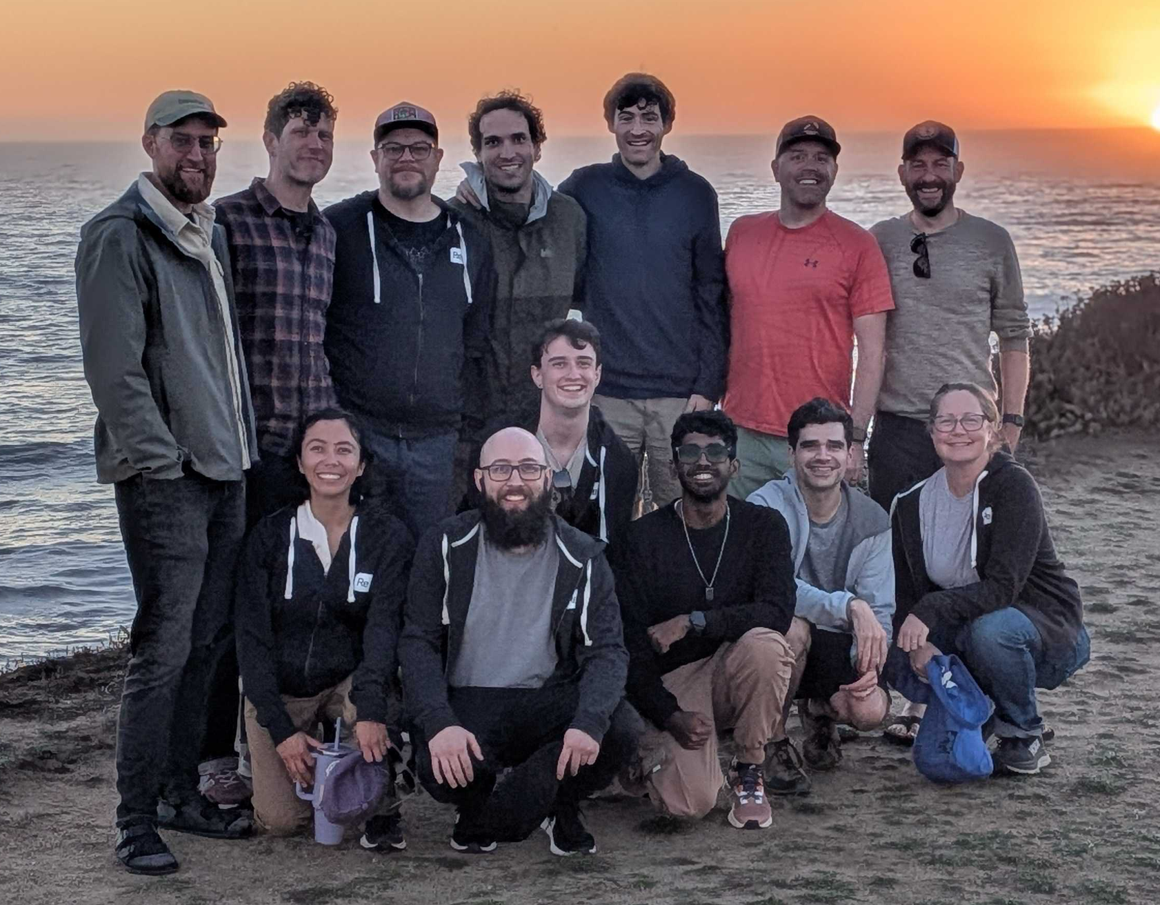 13 SignalFlag team members pose in front of a sunset after a team hike along the coast in California